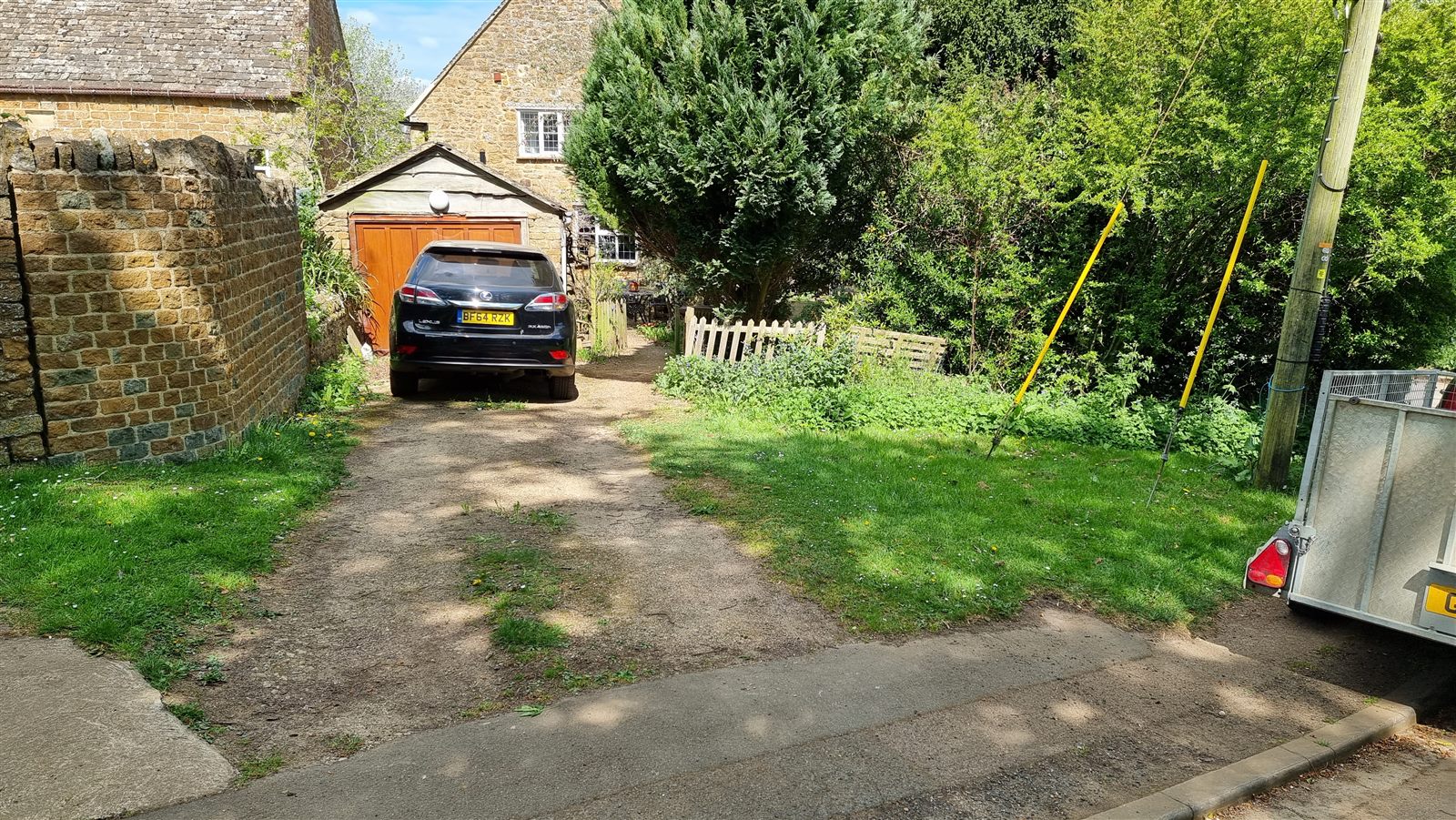 Driveway and established garden before clearance, with dense shrubs beside the stone cottage.
